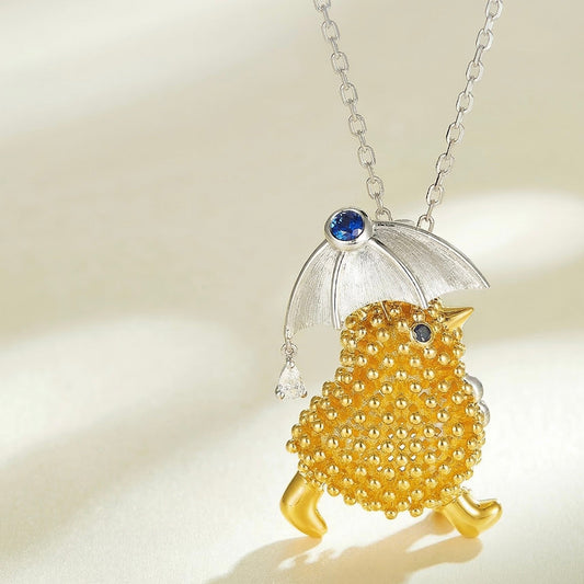 Gold bird pendant with clear umbrella and blue gemstones on a beige background