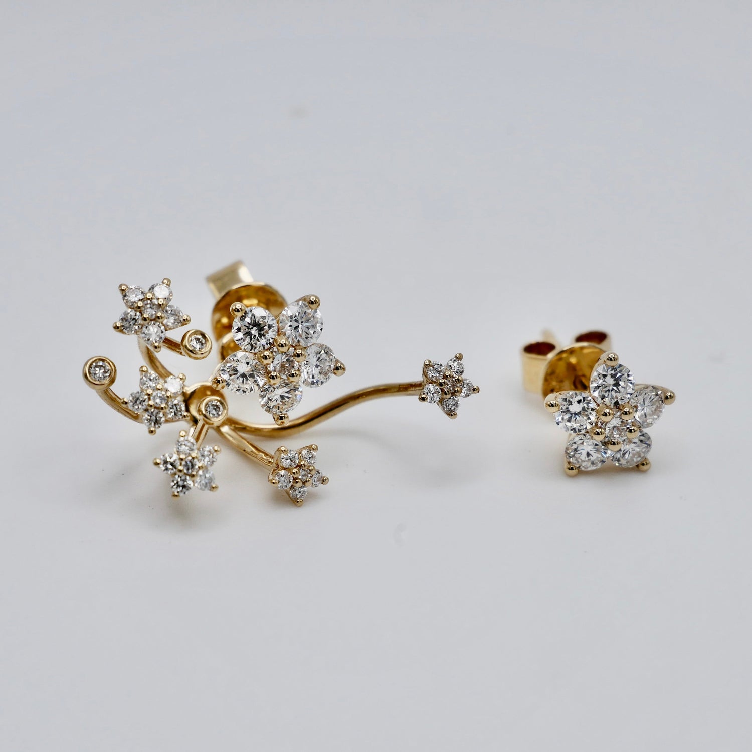 A pair of gold branch-shaped stud earrings with multiple starburst clusters of clear gemstones, displayed on a light gray background.