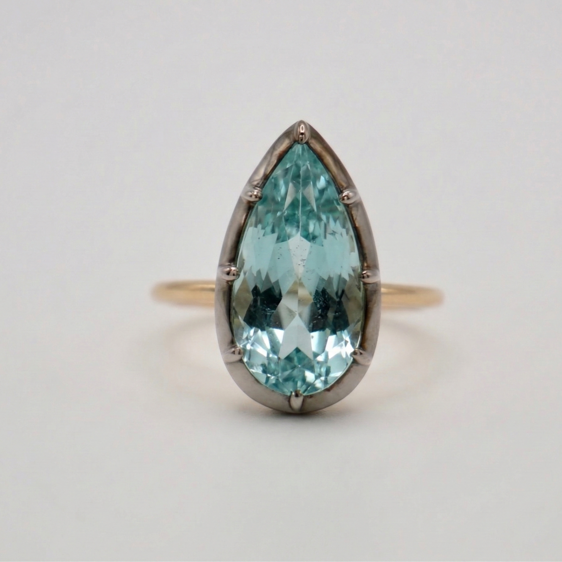 Ring with a teardrop-shaped blue gemstone on a light gray background