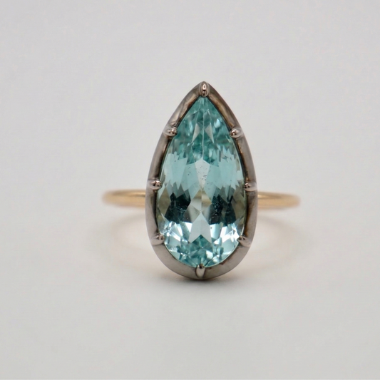 Ring with a teardrop-shaped blue gemstone on a light gray background
